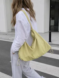 Detail view of large capacity nylon hobo shoulder bag in light yellow worn outdoors.