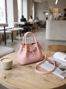 Detail view of the stylish pink leather handbag featuring a chic belt design on wooden table.