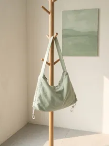 Minimalist green nylon hobo bag hanging on wooden rack in soft light scene detail shot