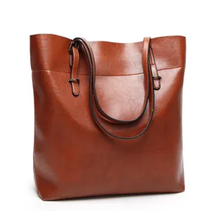 Brown leather tote bag detail showing fine texture, double straps, and metal hardware.