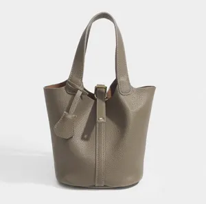 Classic minimalist taupe PU leather bucket handbag with double top handles and chic central strap.