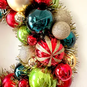 Nahaufnahme des Weihnachtskranzes mit bunten roten, grünen und goldenen Kugeln sowie Lametta.