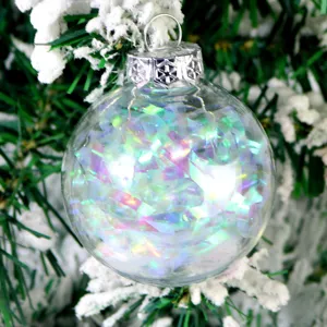 Detailaufnahme der transparenten Weihnachtskugel mit Lametta und verschneitem Ast.