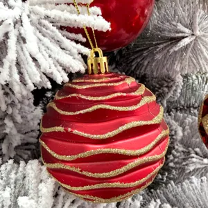 Nahaufnahme einer roten Weihnachtskugel mit Goldglitzerwellen am geschmückten Tannenbaum.