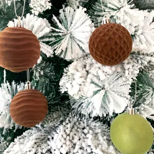 Nahaufnahme beflockter Christbaumkugeln an schneebedeckten Zweigen mit strukturierter Optik.