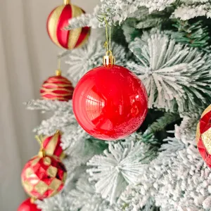 Detaillierte Nahaufnahme von roten und goldenen Christbaumkugeln an schneebedeckten Zweigen.