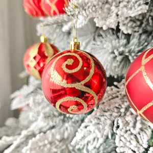 Nahaufnahme einer roten Weihnachtskugel mit Goldglitter am beflockten Tannenbaum.