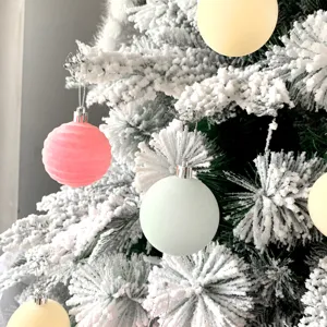 Nahaufnahme von beflockten Christbaumkugeln an verschneiten Zweigen, pastellfarbene Deko.
