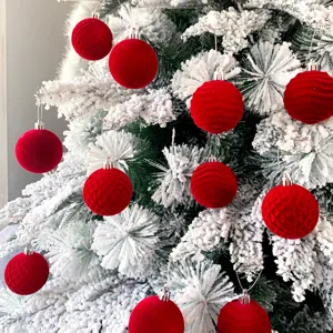 Nahaufnahme von roten Samt befleckten Weihnachtskugeln an schneebedeckten Tannenzweigen.