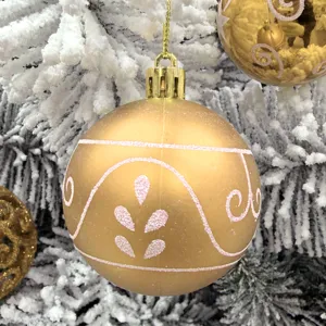 Nahaufnahme einer goldenen Christbaumkugel mit rosa Glitzer auf verschneitem Ast.