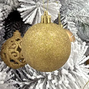 Nahaufnahme einer funkelnden goldenen Glitzer Weihnachtskugel an schneebedeckten Tannenzweigen.