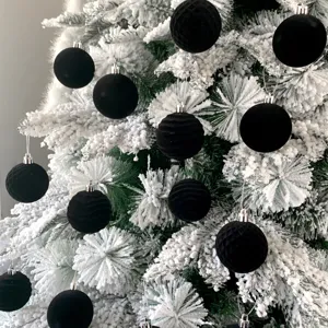 Nahaufnahme von schwarzen beflockten Christbaumkugeln hängend an schneebedeckten Ästen.