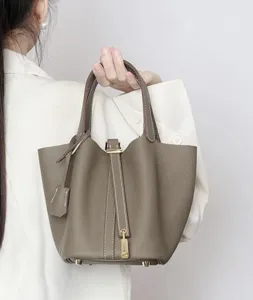 Close-up detail of the stylish taupe bucket handbag, featuring handles and golden lock.