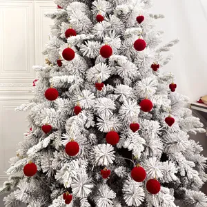Flockter weißer Weihnachtsbaum dekoriert mit roten Samtkugeln und Herzornamenten für Festtage.