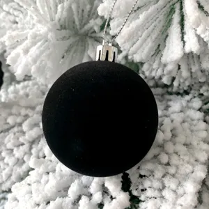 Detailaufnahme einer schwarzen beflockten Christbaumkugel hängend am verschneiten Ast.