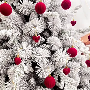 Nahaufnahme der beflockten weißen Weihnachtsbaumzweige mit edlen roten Samtkugeln und Herzen.