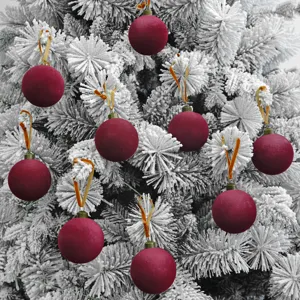 Nahaufnahme von dunkelroten Samt Weihnachtskugeln hängend an einem schneebedeckten Baum.