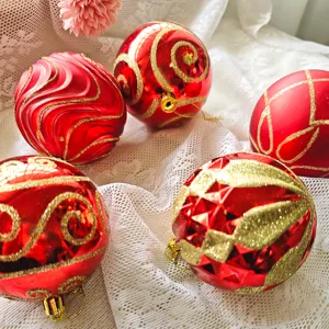 Nahaufnahme von roten und goldenen Glitzer Weihnachtskugeln auf weißem Spitzenhintergrund.
