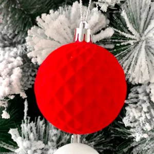 Nahaufnahme einer roten beflockten Weihnachtskugel mit Muster an schneebedecktem Ast.