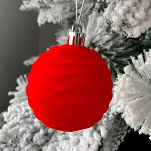 Nahaufnahme Detail einer roten beflockten Christbaumkugel hängend an schneebedeckten Ästen.