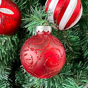 Nahaufnahme von festlichen roten Christbaumkugeln mit Glitzer am grünen Tannenbaum.