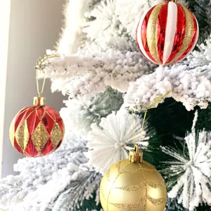 Nahaufnahme glänzender roter und goldener Weihnachtskugeln an schneebedeckten Ästen.