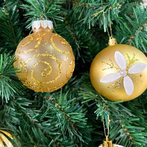 Detaillierte Nahaufnahme von goldenen Weihnachtskugeln, die an einem grünen Zweig hängen.
