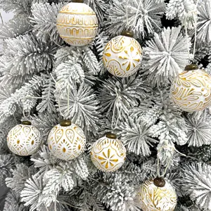 Nahaufnahme Detail von weiß gold geprägten Weihnachtskugeln an einem geschneiten Tannenbaum.