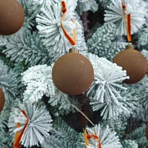 Detailaufnahme der braunen beflockten Weihnachtskugel an verschneiten Zweigen.
