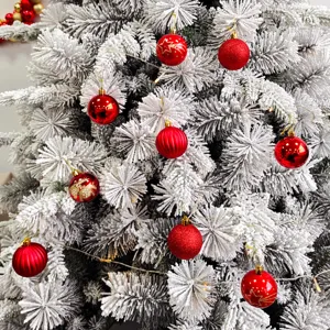 Nahaufnahme eines beflockten Weihnachtsbaumes mit roten Kugeln und festlicher Lichterkette.