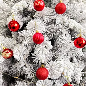 Nahaufnahme eines beflockten weißen Weihnachtsbaums mit roten Kugeln und Lichterkette.