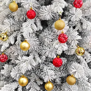 Nahaufnahme festlicher roter und goldener Christbaumkugeln an beflockten Tannenzweigen.