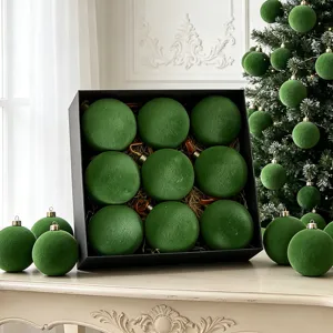 Detailansicht grüner beflockter Christbaumkugeln in schwarzer Geschenkbox und Weihnachtsbaum.