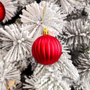Nahaufnahme einer klassischen roten gerippten Christbaumkugel an frostigen Tannenzweigen.