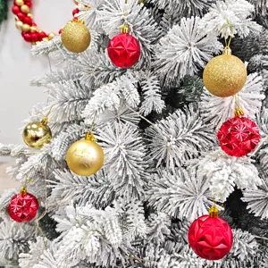 Nahaufnahme verschneiter Weihnachtsbaumzweige, dekoriert mit roten und goldenen Kugeln.