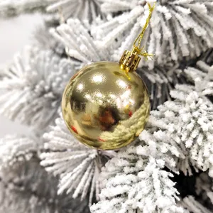 Nahaufnahme einer glänzenden goldenen Christbaumkugel an schneebedeckten Tannenzweigen.