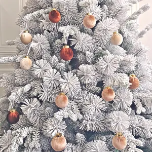Nahaufnahme des beflockten Weihnachtsbaumes, dekoriert mit luxuriösen Samt-Christbaumkugeln.