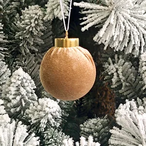 Detailaufnahme einer stoffbezogenen champagnerfarbenen Christbaumkugel am verschneiten Baum.