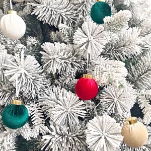Detailaufnahme von farbigen Samt-Weihnachtskugeln an den schneebedeckten Zweigen des Tannenbaumes.