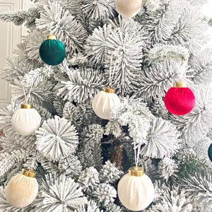 Detailaufnahme von Weihnachtskugeln aus Samt hängend an schneebedeckten Kiefernzweigen.