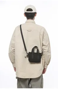 Back view detail of a model wearing a small black commuter crossbody bag with top handles