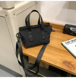 Detailed view of a small black nylon crossbody bag on a wooden desk next to a vintage camera