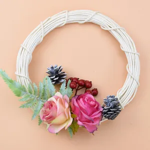 Detailed view of white wicker wreath with artificial roses and pine cones for home decor.