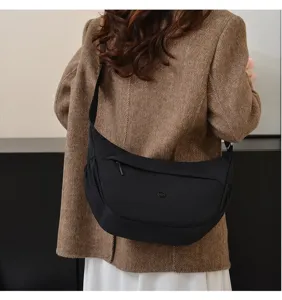 Detail view of the black minimalist crescent shoulder bag worn on model, showing shape and strap.