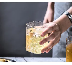Transparenter quadratischer Glasbecher mit goldenen Buchstaben, ideal für Milch und Säfte.