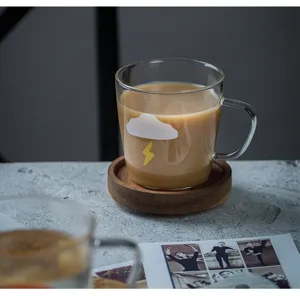 Gros plan d'une tasse à café en verre transparent avec motif nuage et éclair sur table cosy.