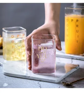 Nahaufnahme eines klaren quadratischen Glasbechers mit goldenen Buchstaben für Säfte und Milch.