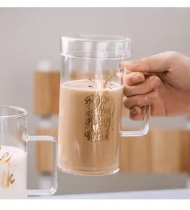 Tasse a cafe en verre transparent avec couvercle et poignee, vue de detail du texte dore.