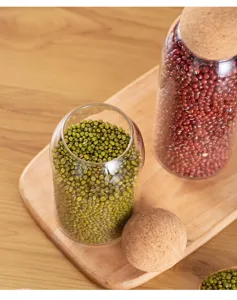 Close-up detail of clear glass storage jar with round cork ball lid filled with green beans.