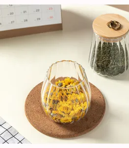Nahaufnahme von transparentem Riffelspenderglas mit getrockneten gelben Blumen auf Korkmatte.